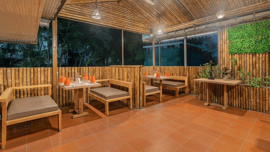 An outdoor or semi-outdoor cafe space at night with wooden furniture, bamboo-style walls, and hanging light fixtures.