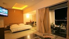 Suite at Pride Biznotel Alkapuri featuring a plush bed next to a large balcony with sitting area and a coffee table along with a TV mounted on the wall