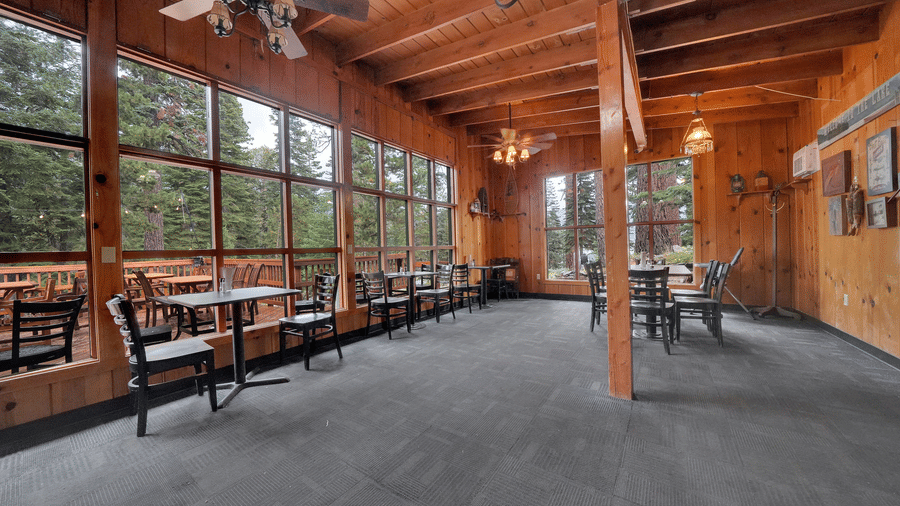 A spacious dining area at Kit Carson Lodge featuring wooden interiors, large windows overlooking the forest, and multiple seating arrangements
