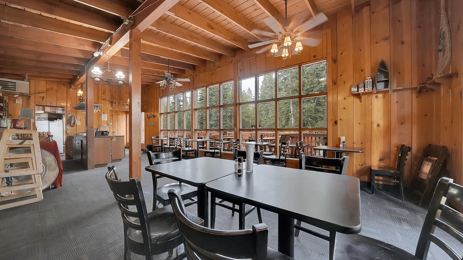 A dining hall at Kit Carson Lodge with wooden walls, ample natural light from wide windows, and tables set up for group dining