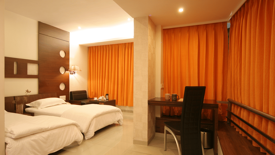 Well-lit Executive Rooms in Pride Biznotel Alkapuri featuring plush beds and a work desk at a distance