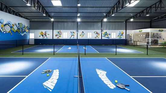 Indoor pickleball courts with paddles and balls on blue surfaces, located at Jenneys Residency, Coimbatore.