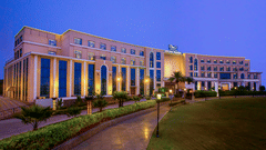 An exterior shot of The Gaurs Sarovar Premiere building at dusk with illuminated columns and landscaping.