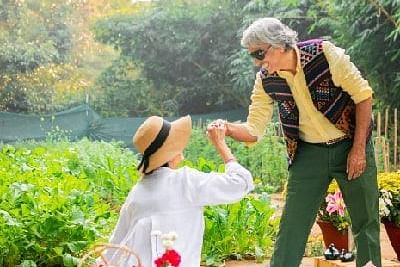 Staff member serving food to a seated guest in the garden area of Karma Chalets during daylight.