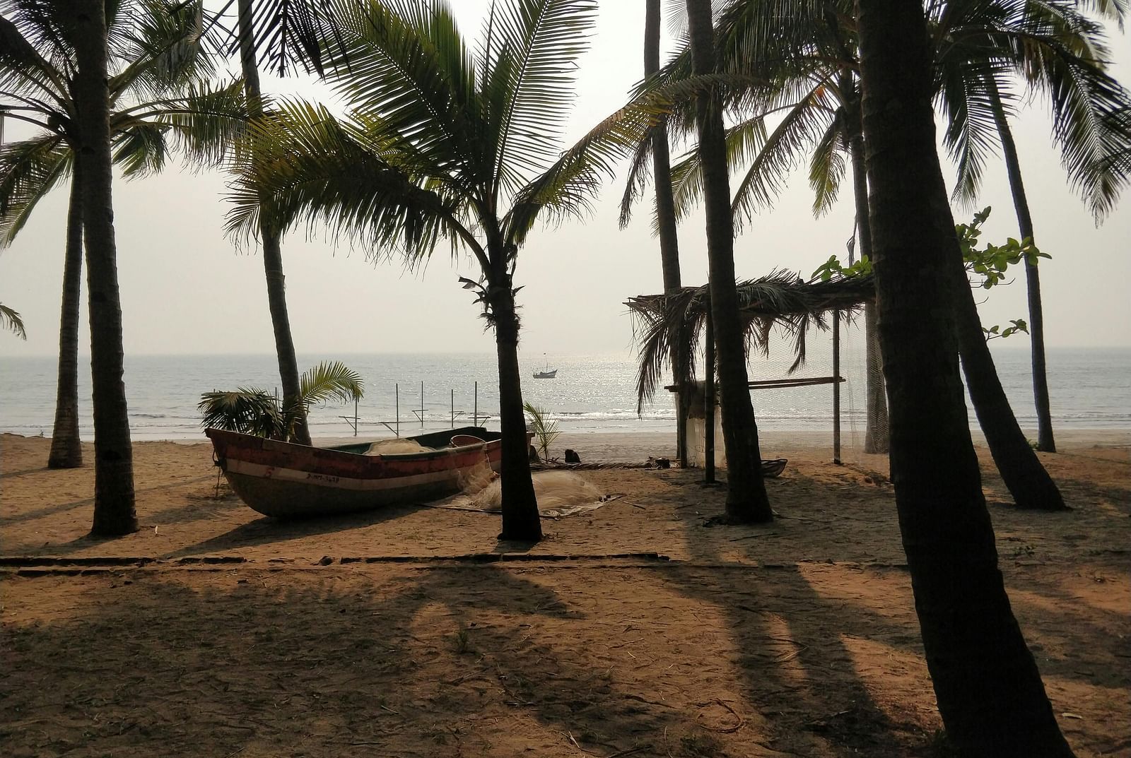 A wooden boat rests on a sandy beach surrounded by palm trees.
