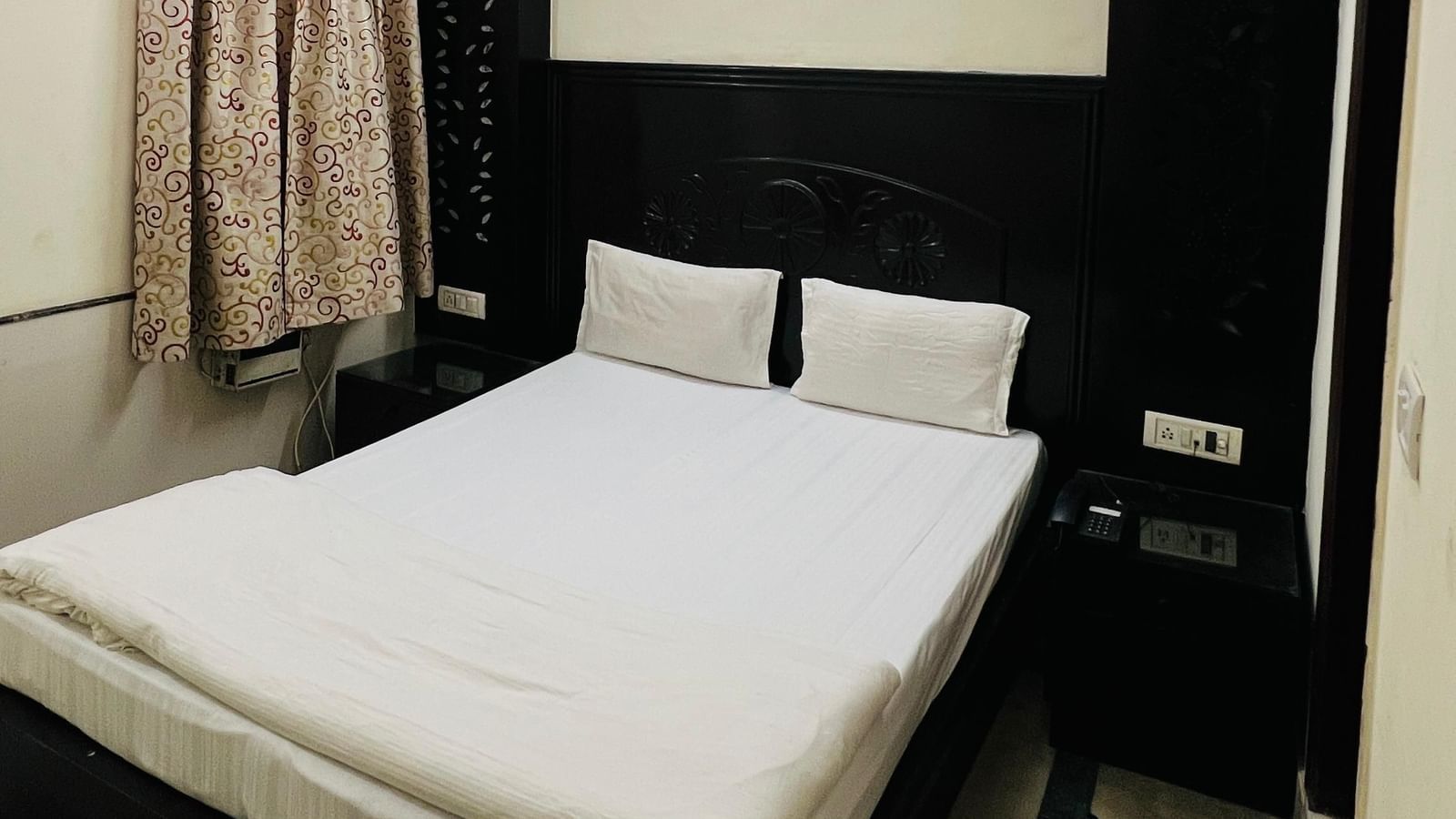 A simple and clean standard room with a comfortable bed, a ceiling fan, and dark wood furniture, offering basic amenities for a restful stay at Hotel City Palace DX.