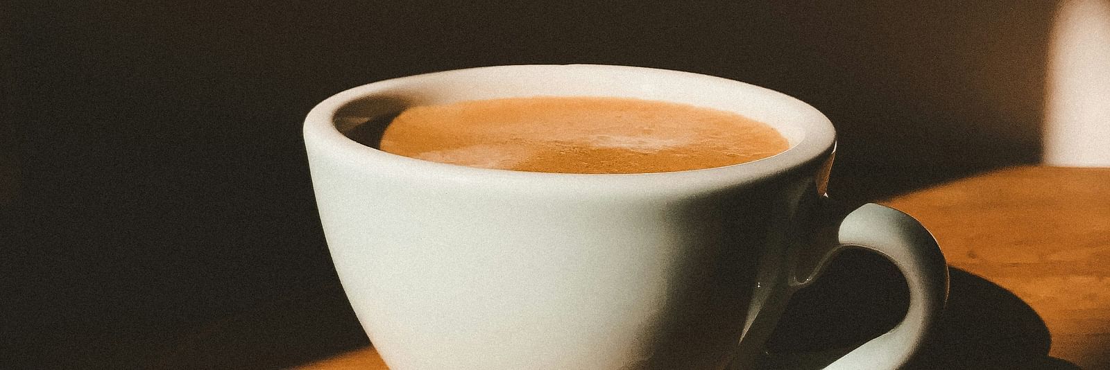 Image of a white coffee cup filled with coffee kept on a brown wall