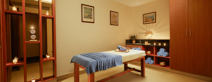Spa room with a massage table, folded cloth, red partition, and storage cabinets - Karur 