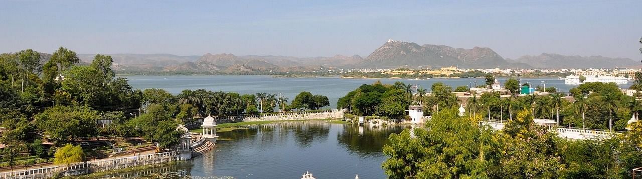 Serene view of Lake Pichola with lush greenery under the blue sky with the backdrop of the hills.