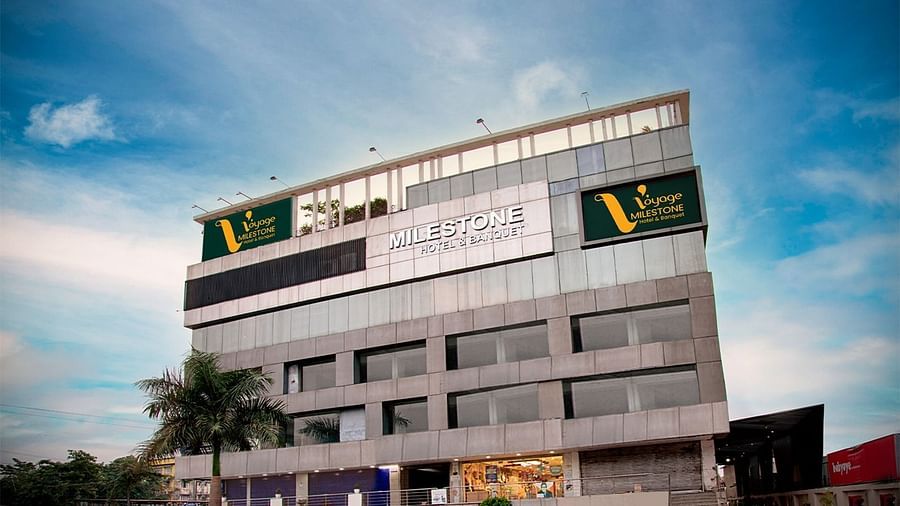 Voyage Milestone Hotel and Banquet is a modern glass and concrete building in Bengaluru, Karnataka, India, under a bright blue sky.
