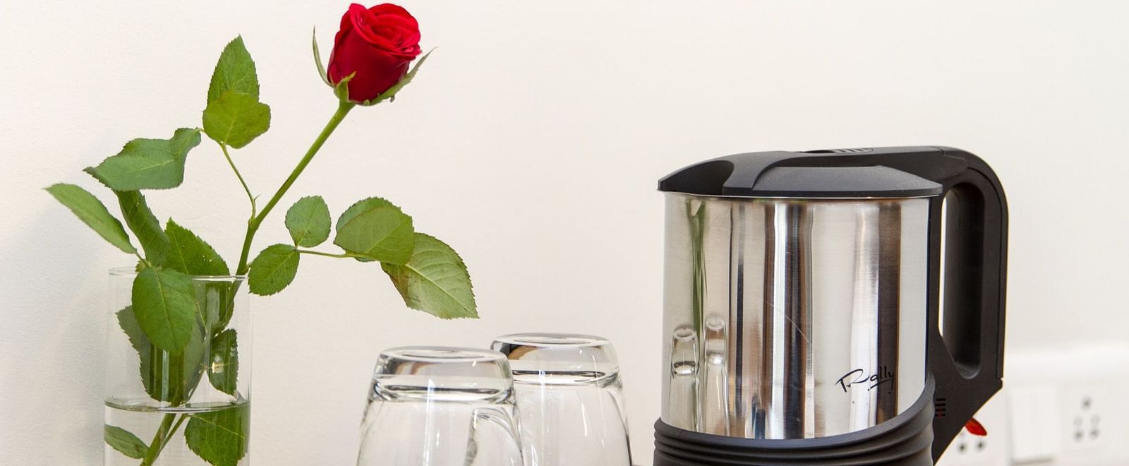 A kettle and glasses placed on a tray and a small vase with a single red rose beside it - Sanctum Suites Whitefield, Bangalore
