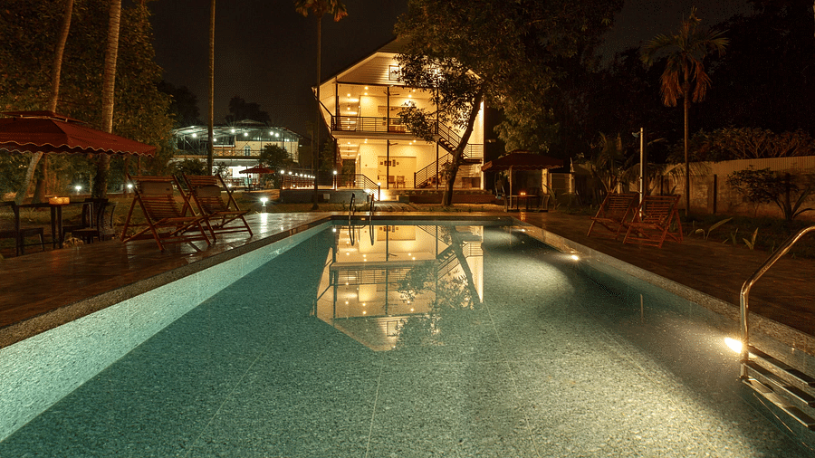 A swimming pool illuminated at night, with buildings and trees visible in the background.