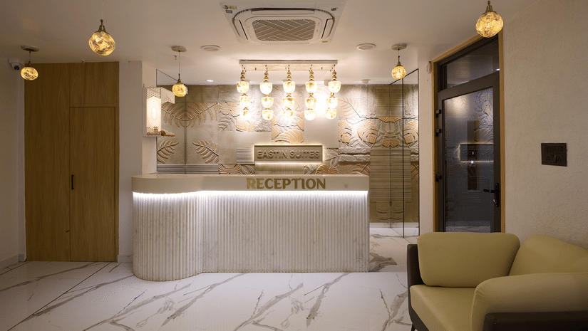 A hotel reception area with a curved white counter, pendant lighting hanging above the counter, and modern marble flooring | Voyage Eastin Suites