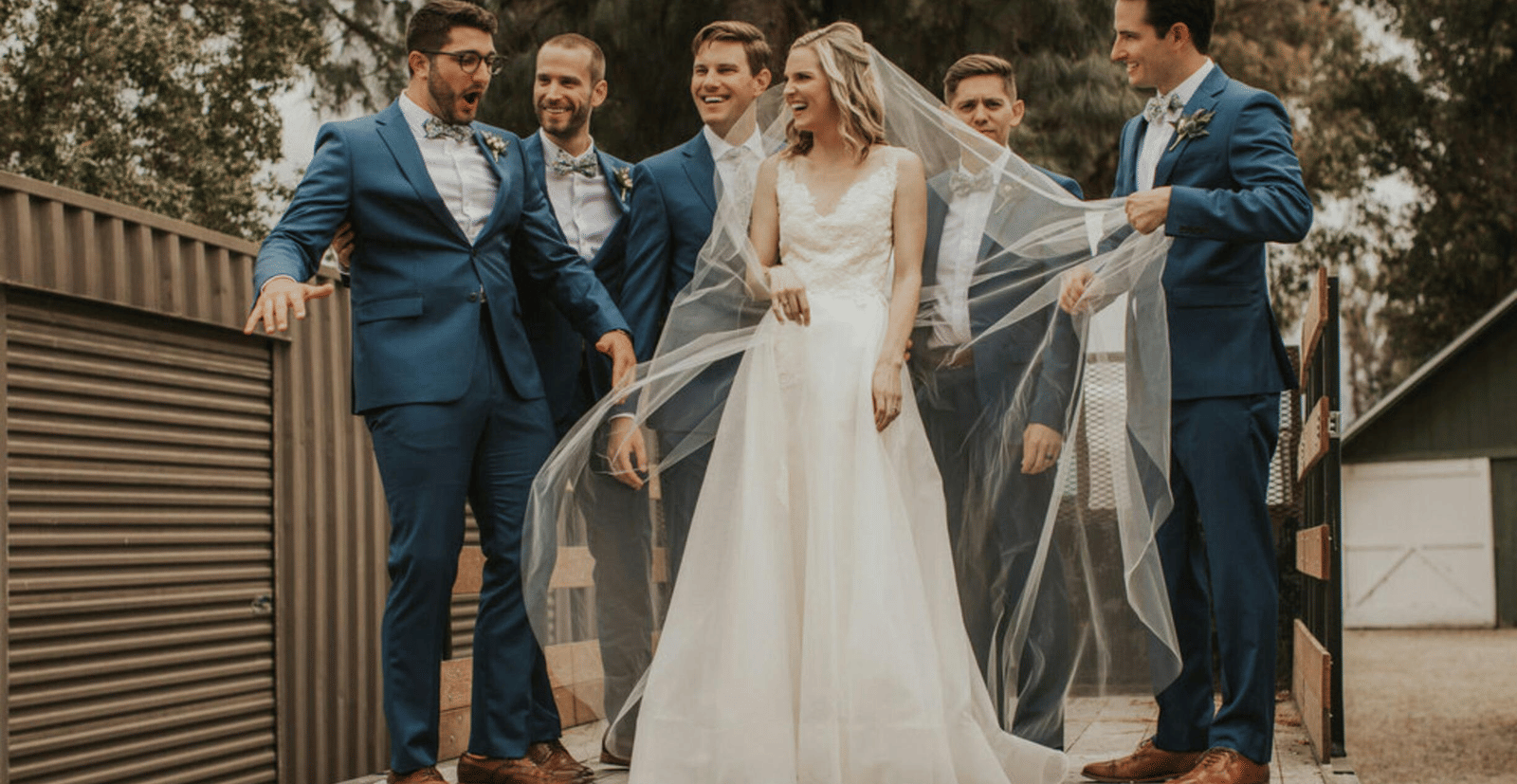 A bride posing for a photo with the groomsmen on a wooden patio