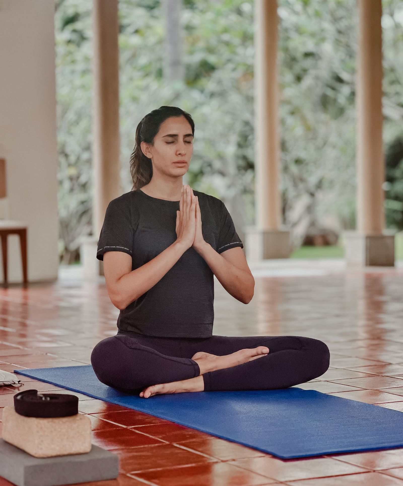 A person doing yoga on a mat in a room with large windows and plants.