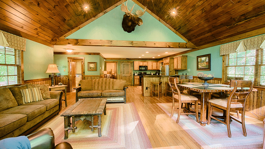 full view image of the living area with a seating area and a dining table along with a decorative stag head hanging above the room - Historic Tapoco Lodge