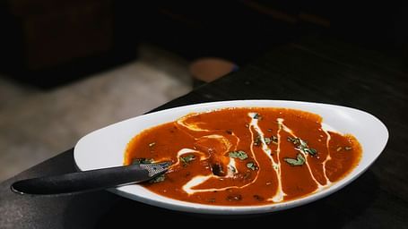 Rich and creamy dal makhani served in a white oval bowl, drizzled with cream and garnished with fresh coriander.