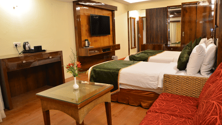 An Executive Triple Room at Benzz Park, Kodaikanal, with modern decor, wooden finishes, and a glass coffee table for added comfort.