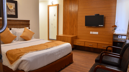 An elegant room in the Family Suite with a bed, wooden furnishing, and a wall-mounted TV for a relaxing stay at Benzz Park, Kodaikanal.