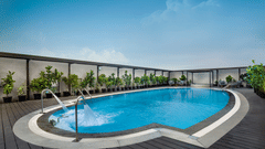 An outdoor swimming pool at The Residency Towers Chennai surrounded by a timber deck and potted plants, with sun loungers visible