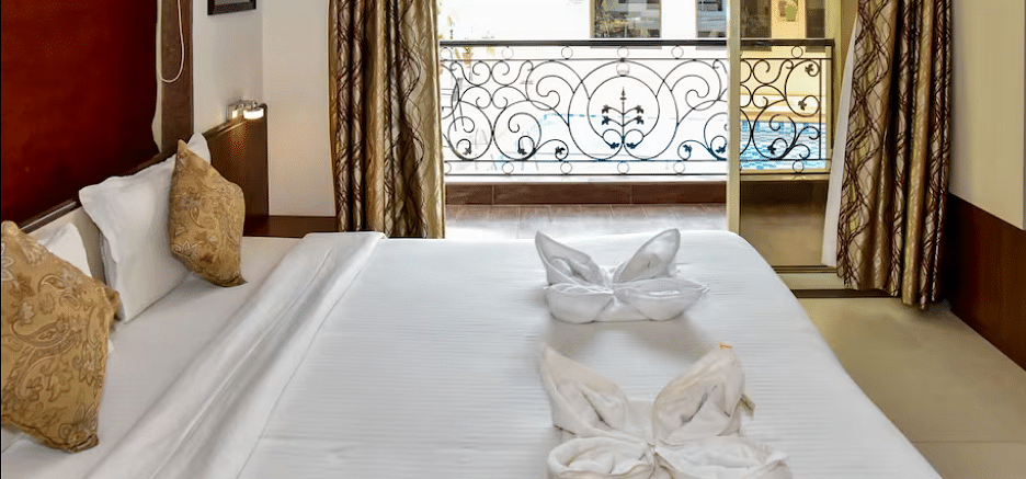 Cosy bedroom with golden cushions, towel swan decor, and a French balcony overlooking greenery at La Vida Studio Inn.