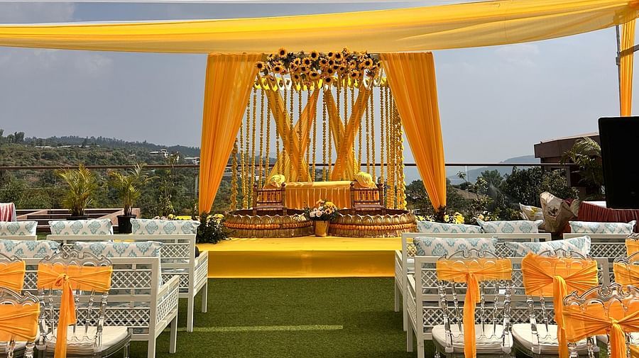 An area decorated with yellow and white fabric pieces, chairs, and a stage decorated with flowers and two seats meant for the bride and groom for their pre wedding rituals at The Grand Legacy Resort & Spa