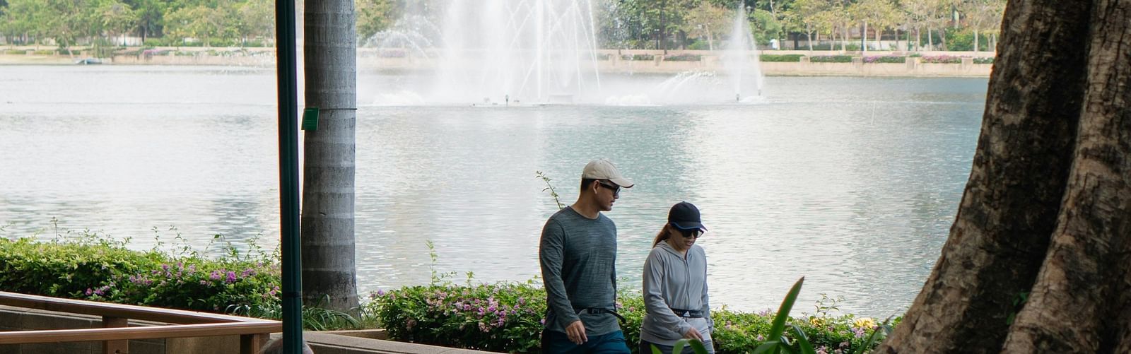 A couple walking on a pathway next to a fountain with trees in the foreground