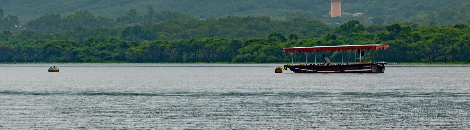 Overview of Fateh Sagar Lake featuring a boat, with mountains in the background partially covered by clouds.
