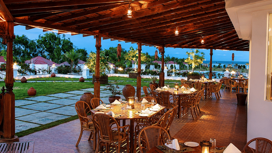 Kapi Multicuisine Restaurant outdoor dining area with wooden beams and warm evening lighting, overlooking a lush garden setting