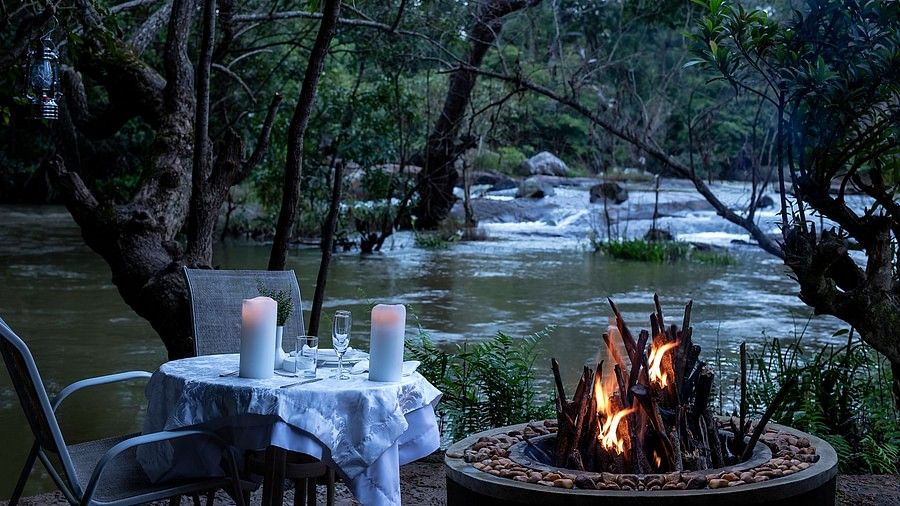 Outdoor candlelit dinner setup by a river in the evening- Amanvana Resort And Spa, Dining in Coorg