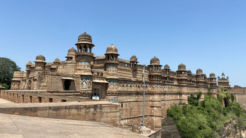 Gwalior Fort showcasing its massive stone walls, intricate architecture, and historic battlements under clear sky.