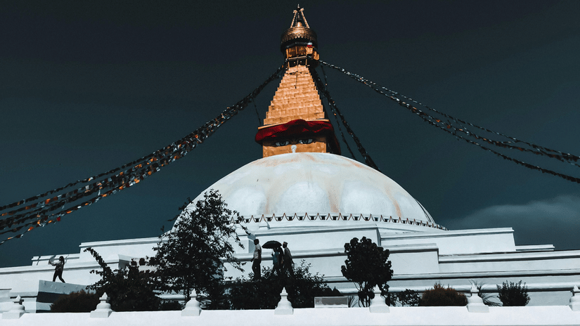 A domed structure with steps, flags, and surrounding area under a dark sky.