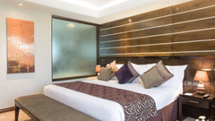 A suite at Boma Inn Eldoret featuring a large bed with multiple cushions, wooden accent wall, warm lighting, bench seating, and contemporary artwork