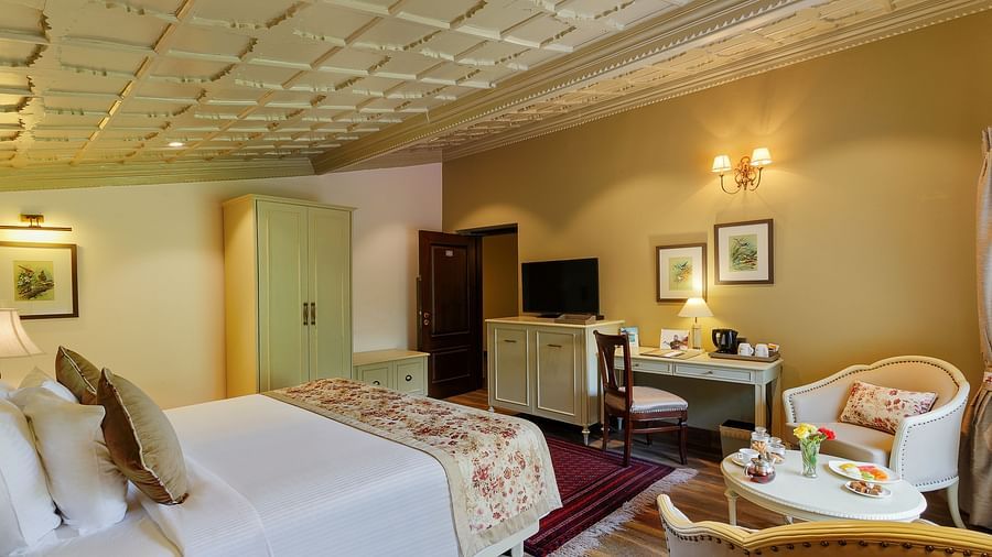 An image featuring a cosy room with decors, king size bed, ceiling designs and framed pictures seen near the flat screen TV - The Naini Retreat