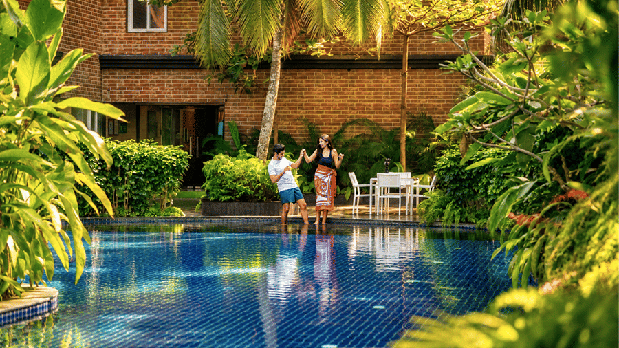 Outdoor swimming pool bordered by lush tropical greenery and resort architecture at MAYFAIR Palm Beach Resort, Gopalpur-on-Sea.   