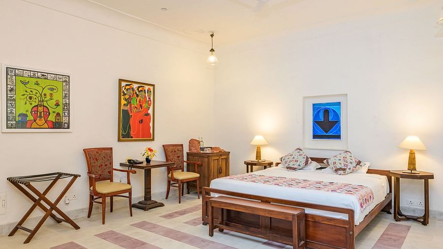Room with bed, patterned pillows and runner, furniture including tables, chairs, and bench, artwork, decorative ceiling light, and patterned floor tiles - Tijara Fort-Palace - 19th Century, Alwar.