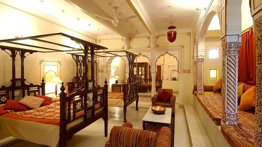 a brightly lit room with a two large beds with a canopy and sofas for sitting - Hotel Castle Mandawar, Jhunjunu
