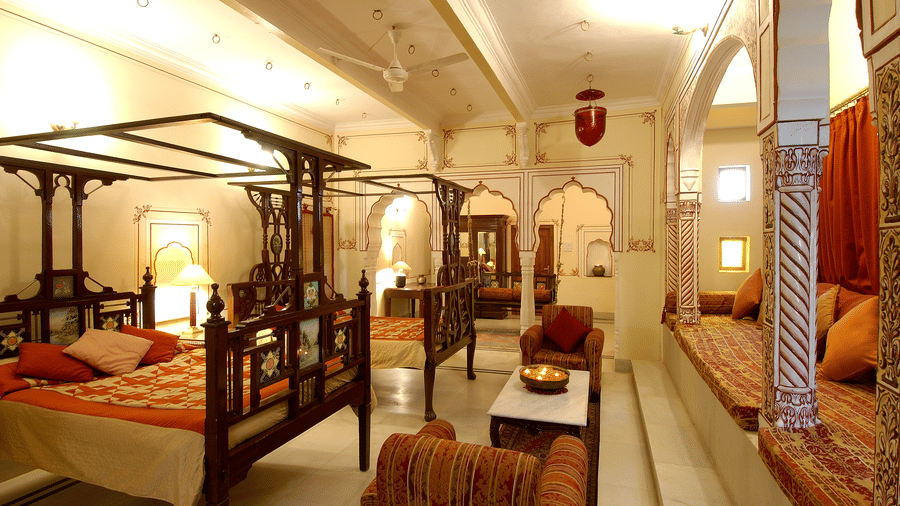 A brightly lit Suite room with a two large beds with a canopy and sofas for sitting at Hotel Castle Mandawa, Jhunjunu