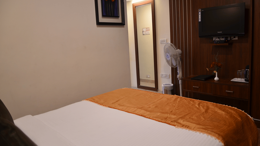A simple room with a single bed, TV, and ambient lighting for a restful solo stay - Benzz Park, Kodaikanal