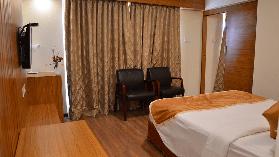 A room in a Family Suite at Benzz Park, Kodaikanal with a plush bed, a TV, and 2 chairs neatly arranged next to a large window.