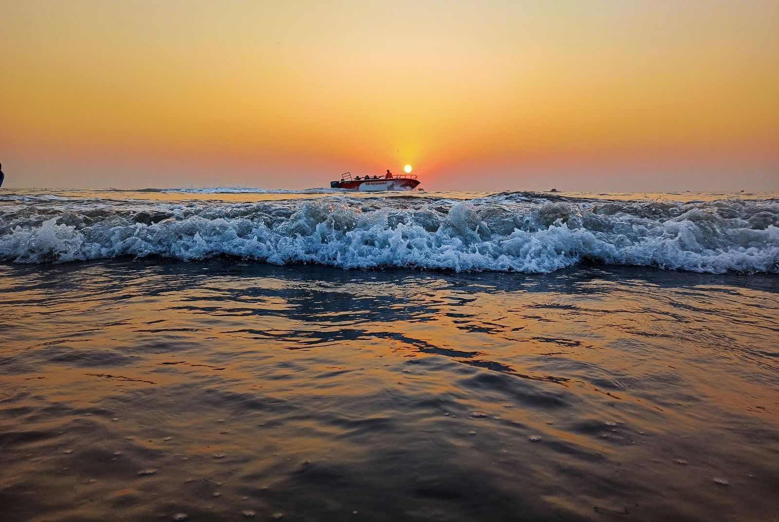 A beautiful sunset over the Arabian sea with gentle waves and a distant ship, capturing a serene coastal view.