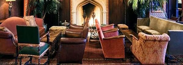 A seating area with 2 sofas, 5 sofa chairs, 2 tea tables, lamps and a fireplace at Hotel Mamallaa Heritage, Mahabalipuram.