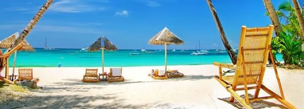 A sandy beach with lounge chairs, umbrellas, and palm trees.