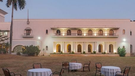A facade image of Jhira Bagh Palace during a sunset with furniture placed in lawn for relaxation