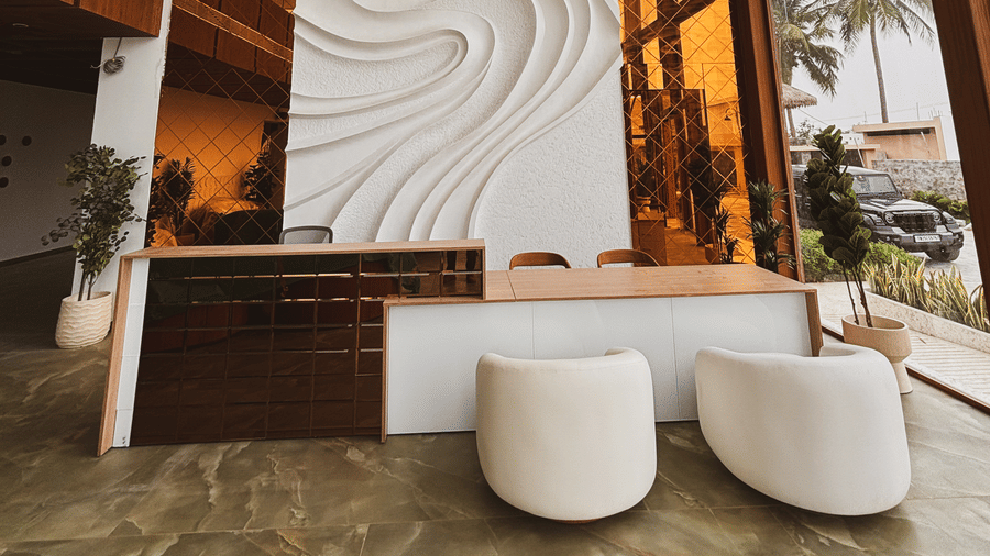 A wide view of the reception area showing a tall wave-patterned wall flanked by orange mirrors and large windows at Avanya Resorts N Retreat.