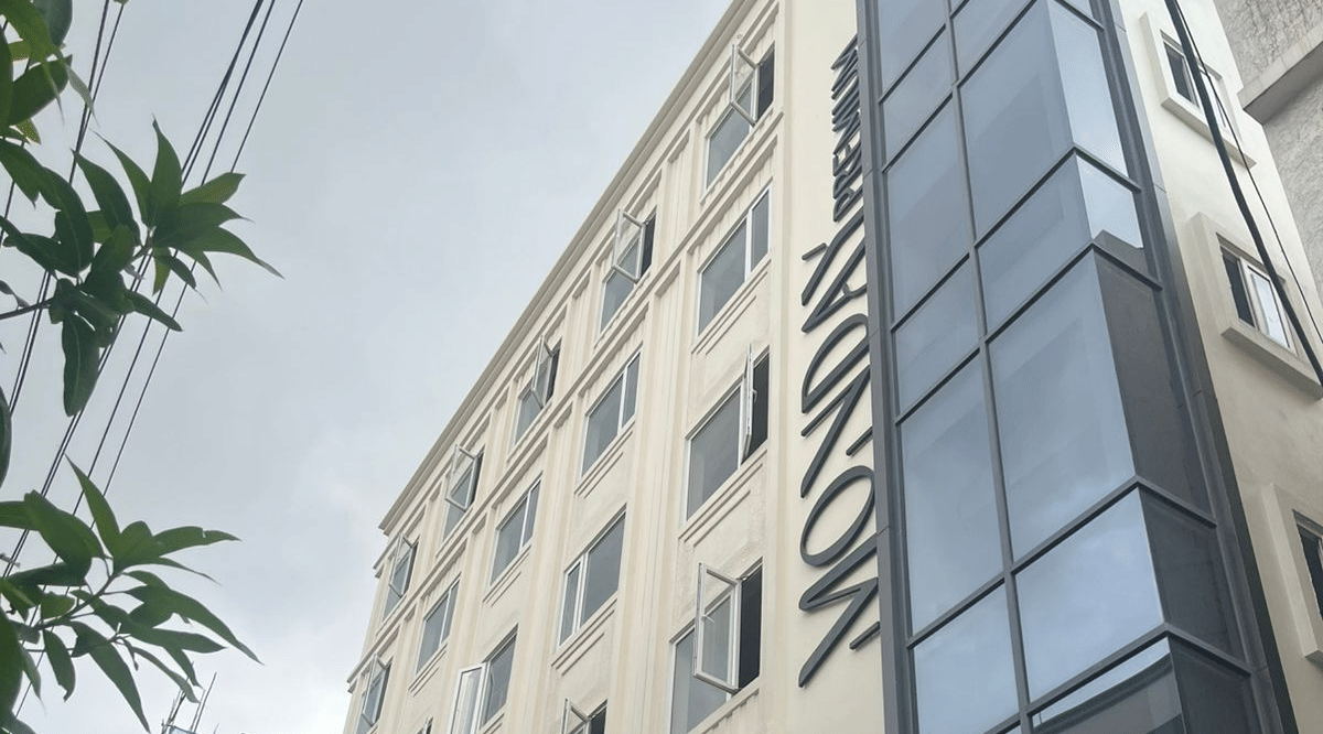  Contemporary exterior view of Monday Premium, Madhapur, showing a multi-storey building with a glass-fronted stairwell and a cream-coloured facade. 