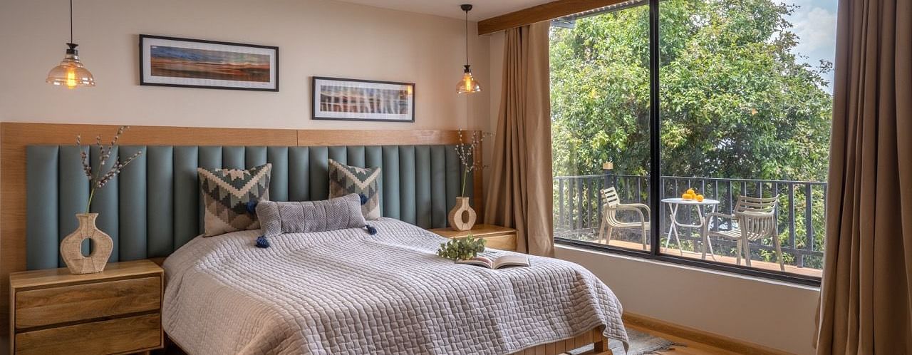 An image of double bedroom with side table a vase and balcony attached to the room | Avalon Cottages, Kanatal