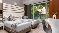  Contemporary room at The Atara, Gurugram featuring two single beds, a white desk, and a balcony view. The room has light wood floors and horizontal wall decor