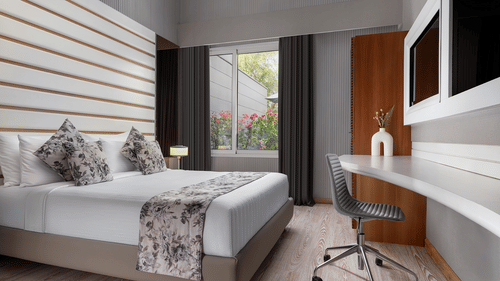A chic room at The Atara, Gurugram with light wood flooring, a neatly made bed, a spacious desk with an office chair, and ample natural light from a large window