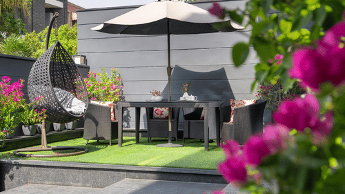 An inviting outdoor patio at The Atara, Gurugram featuring a dining set with an umbrella for shade, surrounded by vibrant blooming flowers and lush green foliage, perfect for relaxation